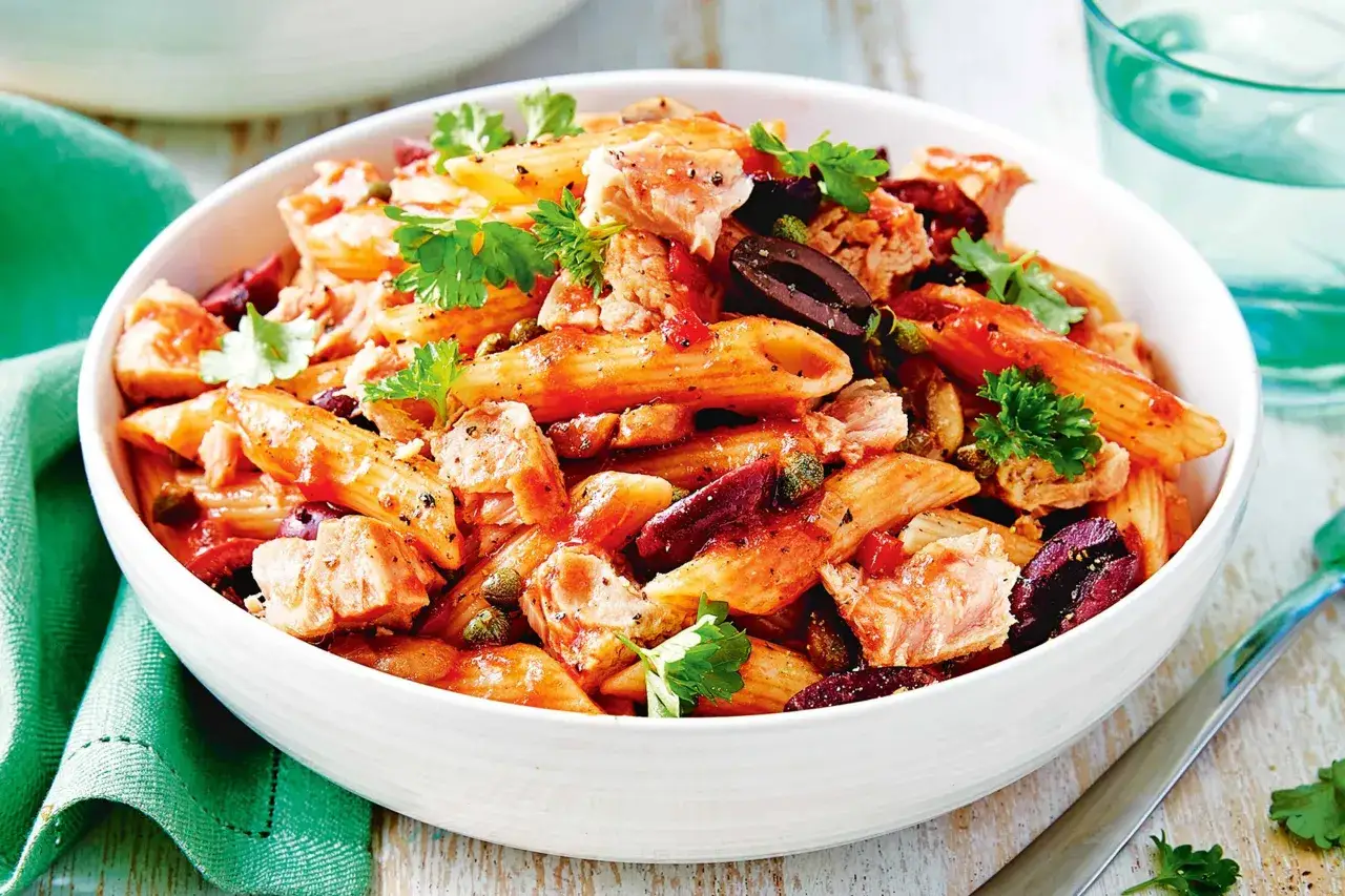 Penne z kawałkami soczystego tonno, oliwkami i kaparami, polane sosem pomidorowym, udekorowane natką pietruszki.