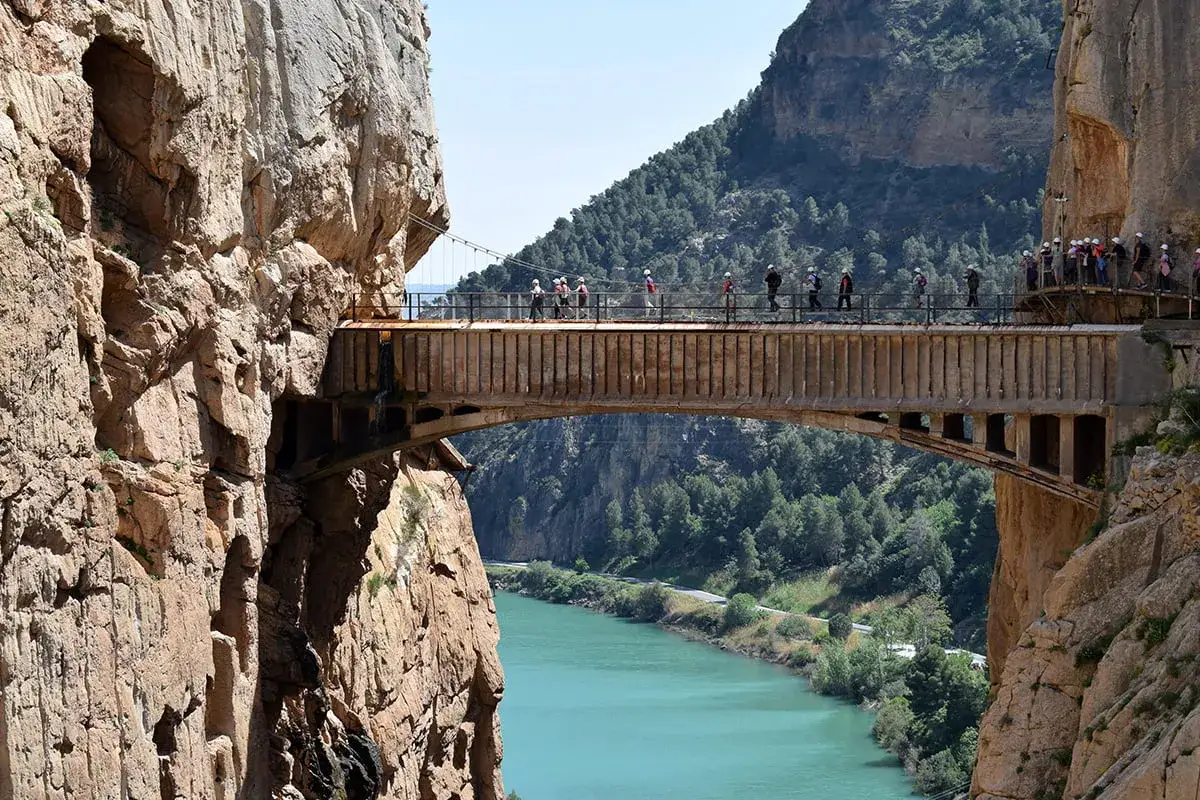 Spacerzy po Caminito del Rey, wąskim szlaku zawieszonym nad turkusową rzeką, wśród stromych, skalistych zboczy.