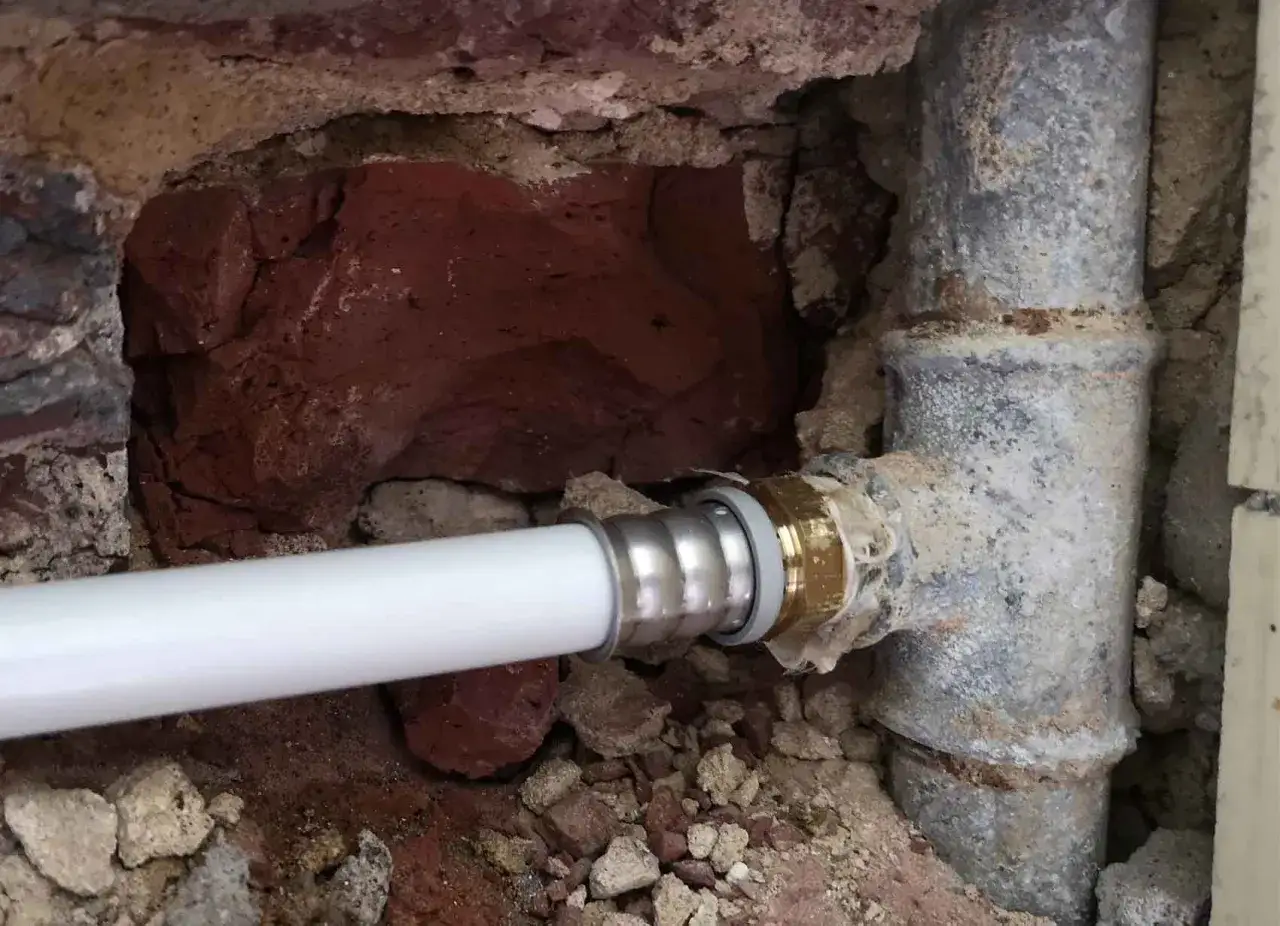 Un nouveau tuyau blanc est raccord&eacute; &agrave; un ancien tuyau de plomb pour l'eau. La ma&ccedil;onnerie est visible autour des canalisations.