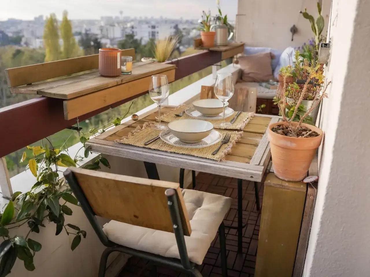 Un balcon filant aménagé pour un repas à deux, avec table, chaises, vaisselle et plantes.