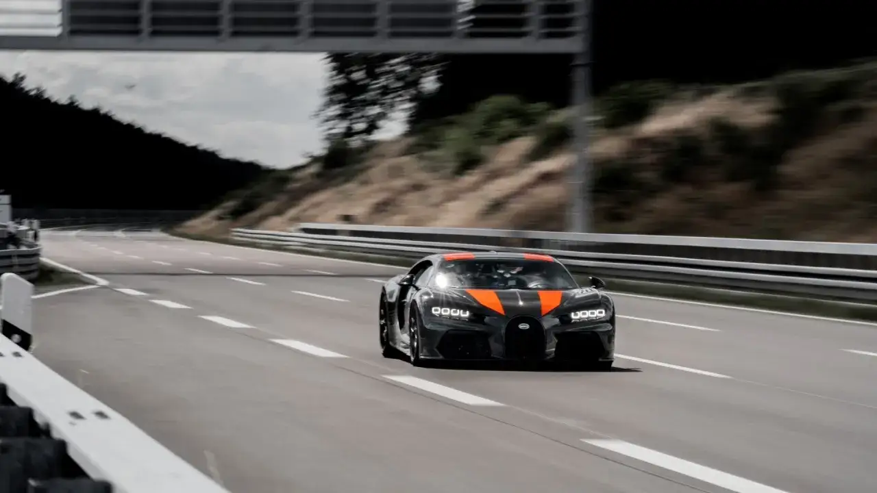 Czarny Bugatti Chiron z pomarańczowymi pasami pędzi po torze, zbliżając się do prędkości 500 km/h.