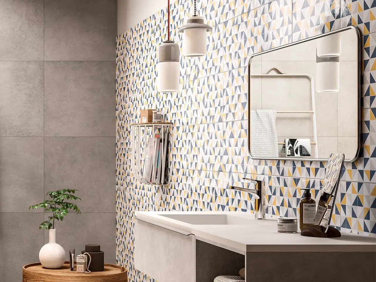 Parete del bagno con piastrelle geometriche colorate e piastrelle grigie. Si vede un lavandino, uno specchio e accessori.