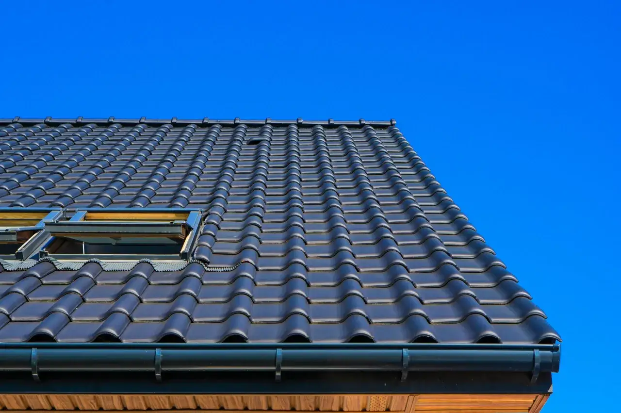 Tetti moderni con tegole scure e lucernari, realizzati con materiali resistenti e di alta qualità, sotto un cielo azzurro intenso.
