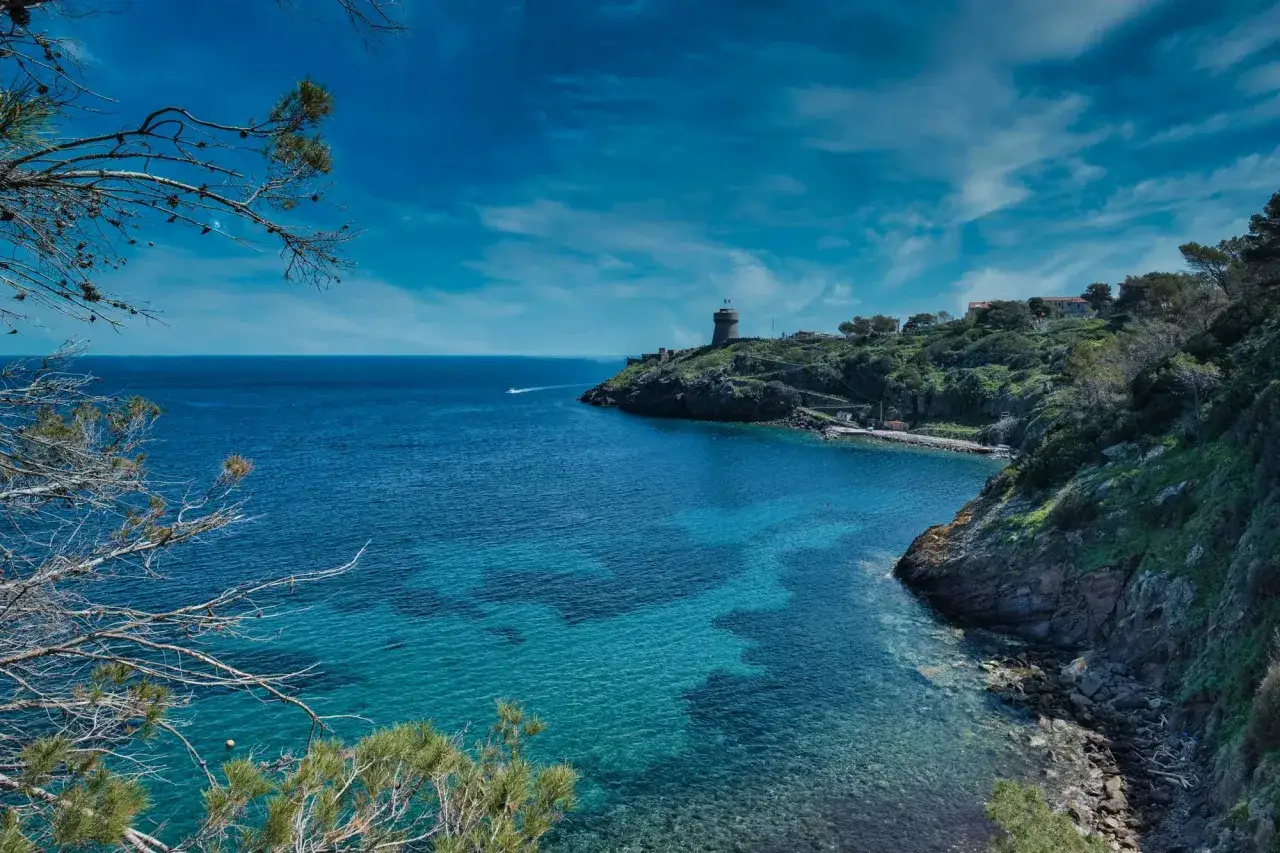 Vista mozzafiato su una baia cristallina di **Capraia isola**, con un faro in lontananza e vegetazione mediterranea.