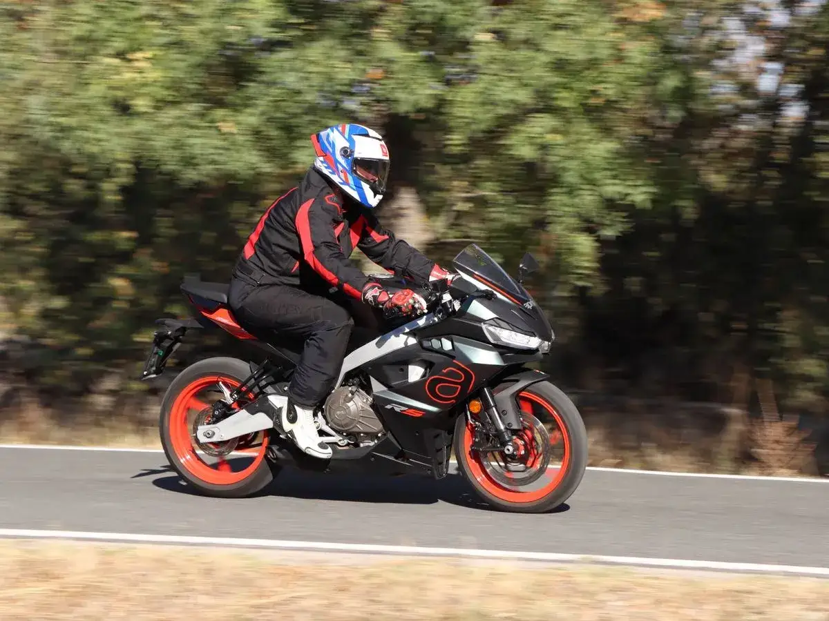 Motociclista en Aprilia RS 457, con detalles de su ficha t&eacute;cnica en mente, recorre una carretera rodeada de &aacute;rboles.