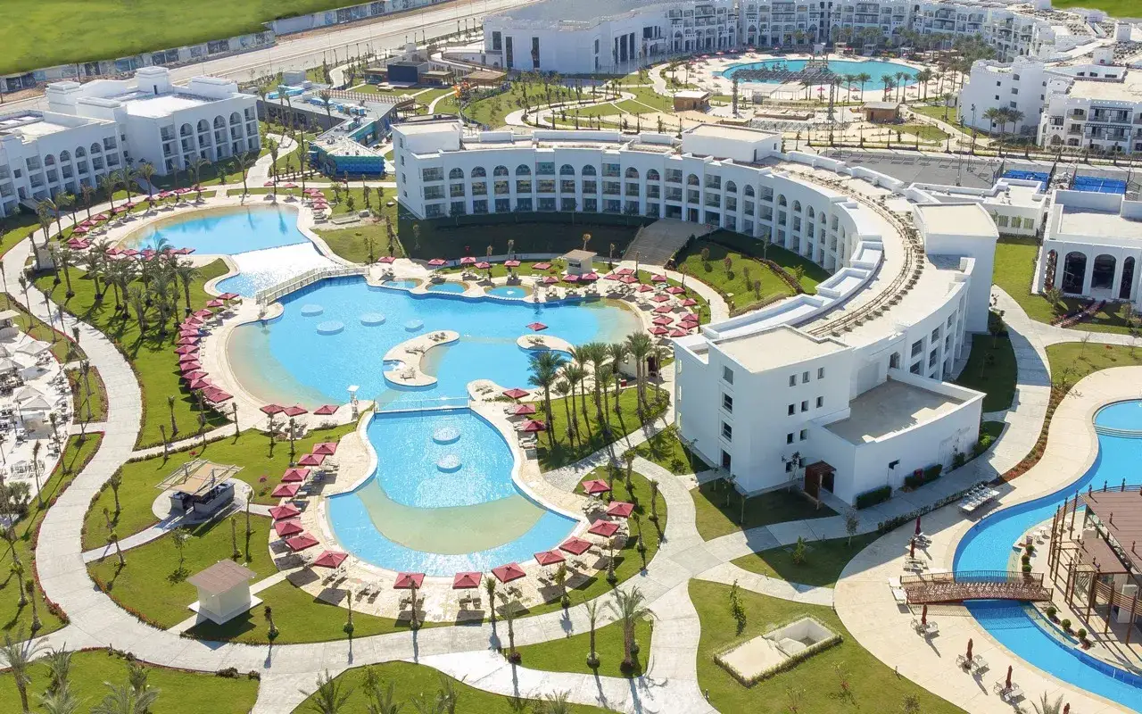 Luksusowy kompleks basenów i budynków hotelowych Rixos Radamis Sharm El Sheikh, otoczony zielenią i palmami, zaprasza na wakacje.