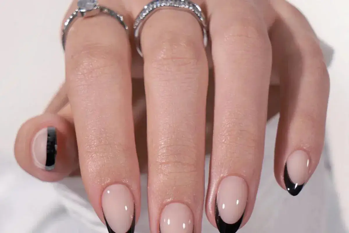 Snygg nagel inspo med fransk manikyr i svart och en nagel med halvmåne-design. Två ringar pryder fingrarna.