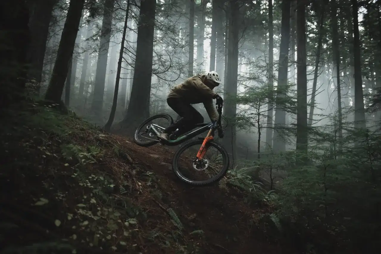 A rider navigates a steep, misty forest trail on an enduro mountain bike, showcasing its rugged design for challenging terrain.
