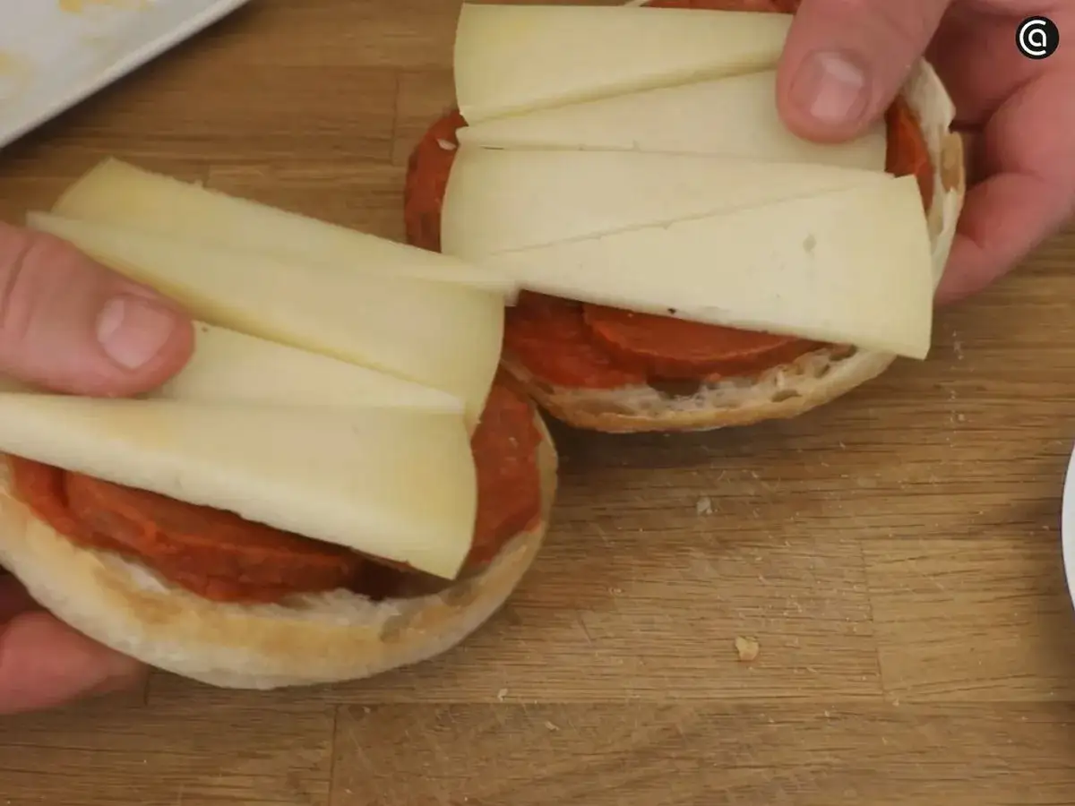 Manos preparando un delicioso panini de queso con chorizo sobre pan rústico.