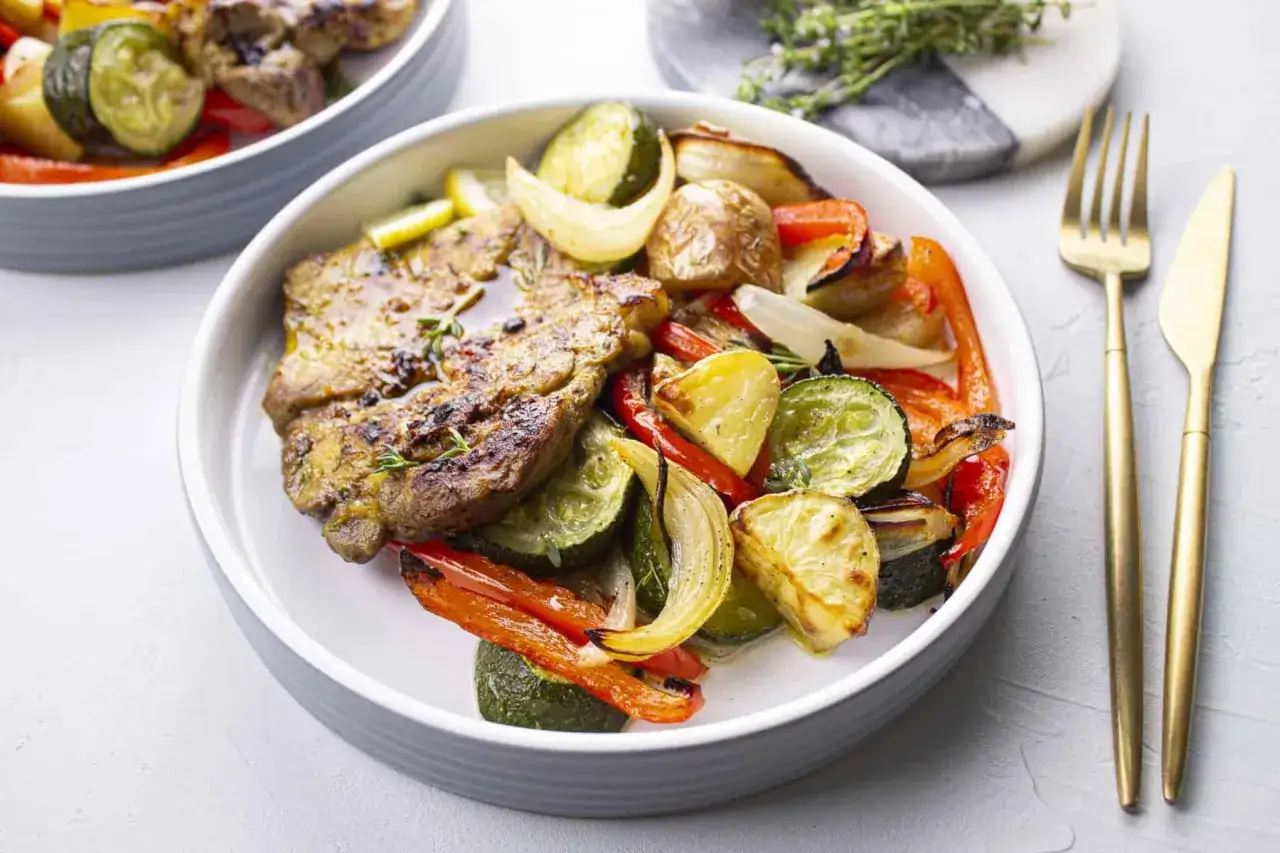 Un plat appétissant d'émincé de porc grillé servi avec des légumes rôtis colorés : courgettes, poivrons, oignons et pommes de terre.