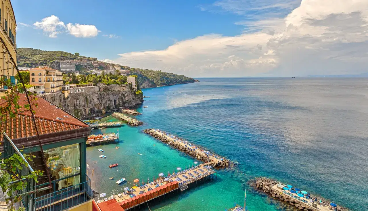 Widok na turkusowe morze i klify z hotelami, plażami i molo. W oddali widać wyspę niedaleko Sorrento.