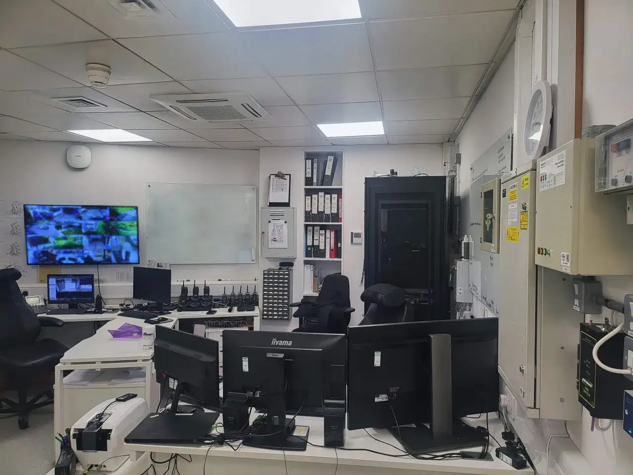 Control room with multiple monitors displaying security feeds, computers, and communication devices, ensuring critical infrastructure security.