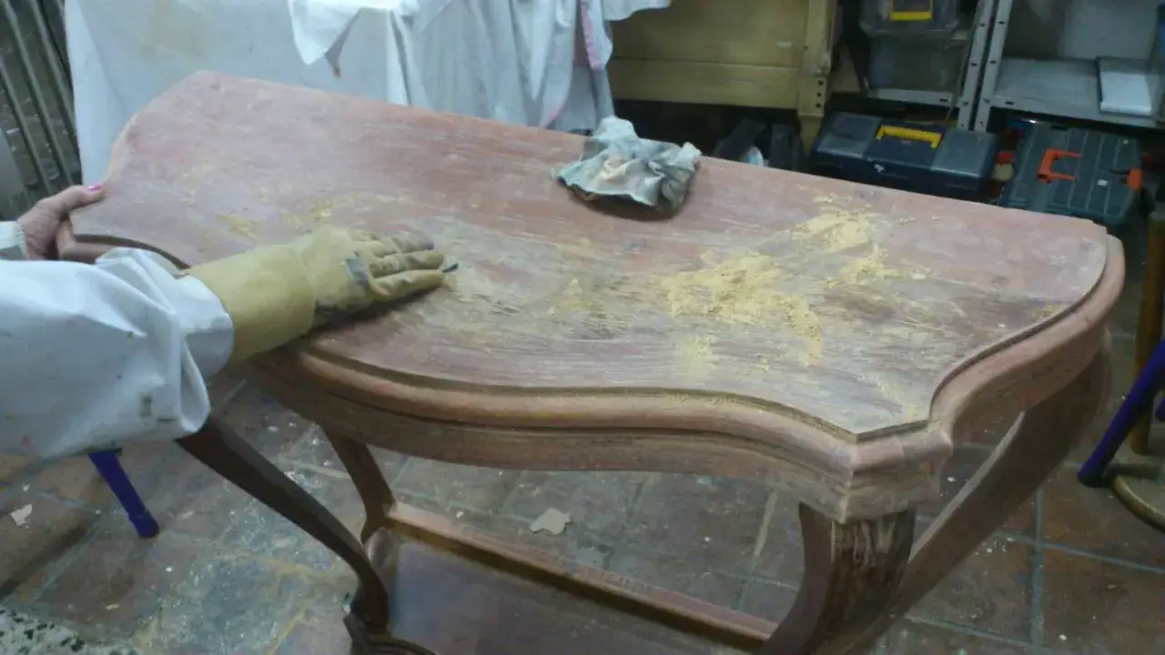 Persona con guante lijando muebles de madera, eliminando pintura vieja para restaurar la superficie.