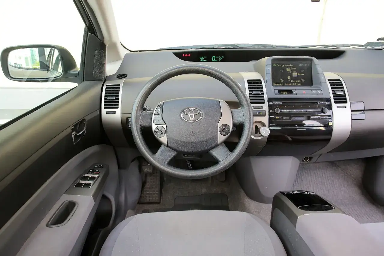 Wnętrze toyoty prius 2: kierownica, deska rozdzielcza z ekranem i radiem, panel drzwi.