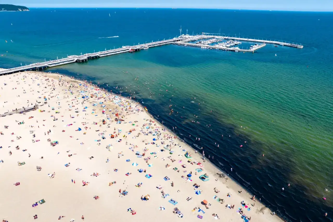 Tłum ludzi na plaży i w wodzie przy najdłuższym molo w Polsce.