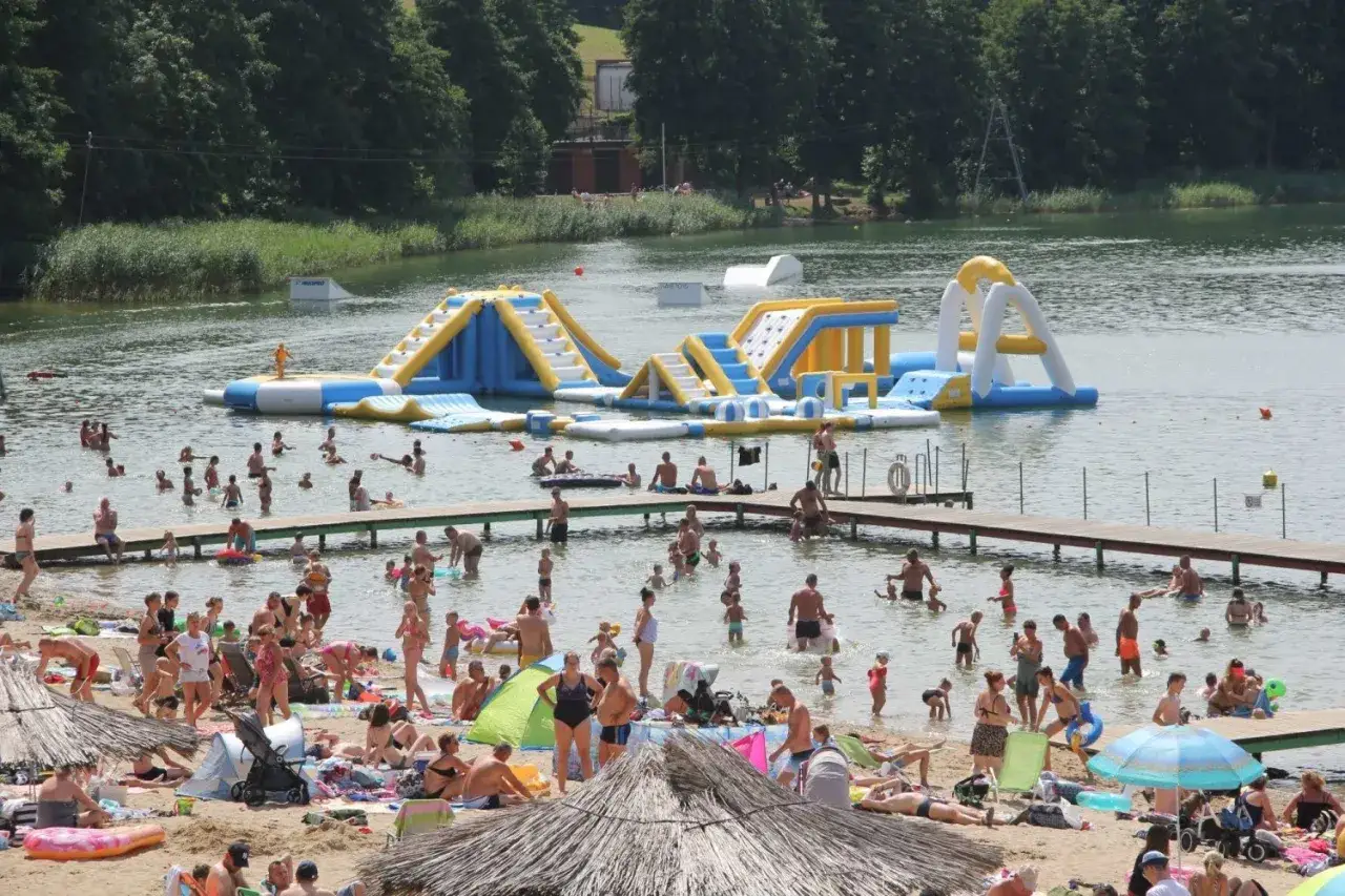 Rodzinny wypoczynek nad jeziorem Jaroszewskim z dmuchanymi atrakcjami wodnymi i plażą pełną słońca.