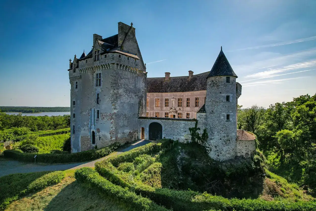 Le majestueux **ch&acirc;teau du Bouchet** se dresse fi&egrave;rement sur une colline verdoyante, dominant un lac paisible sous un ciel bleu &eacute;clatant.