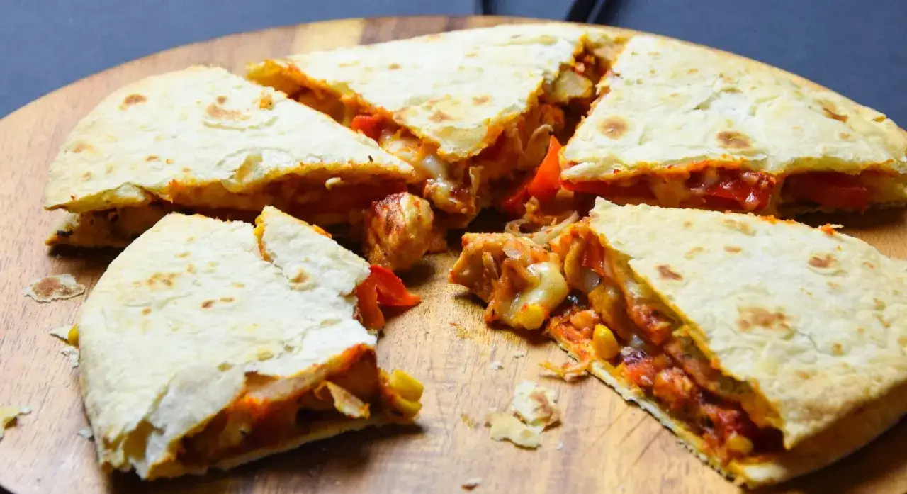 Pyszna quesadilla z kurczakiem, papryką i roztopionym serem, pokrojona na trójkąty i ułożona na drewnianej desce.
