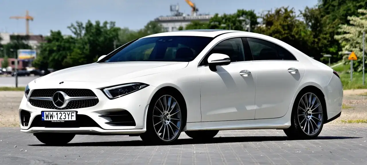 Biały Mercedes CLS na tle drzew i budynków. Poznaj szczegółowe mercedes cls dane techniczne tego eleganckiego sedana.