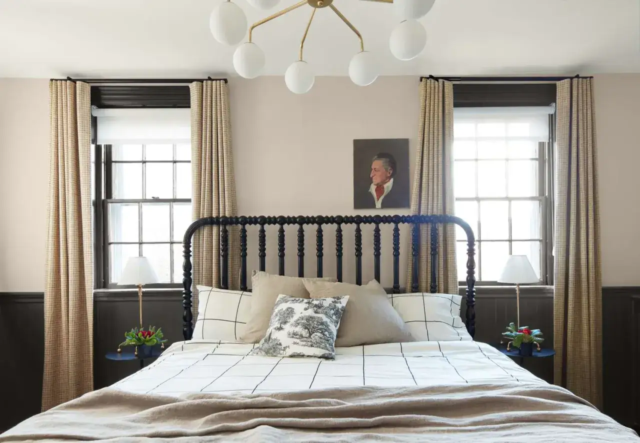 Gem&uuml;tliche wandgestaltung mit warmen schlafzimmer farben. Ein Bett mit schwarzem Kopfteil, karierten Vorh&auml;ngen und einem Portr&auml;t &uuml;ber dem Bett.