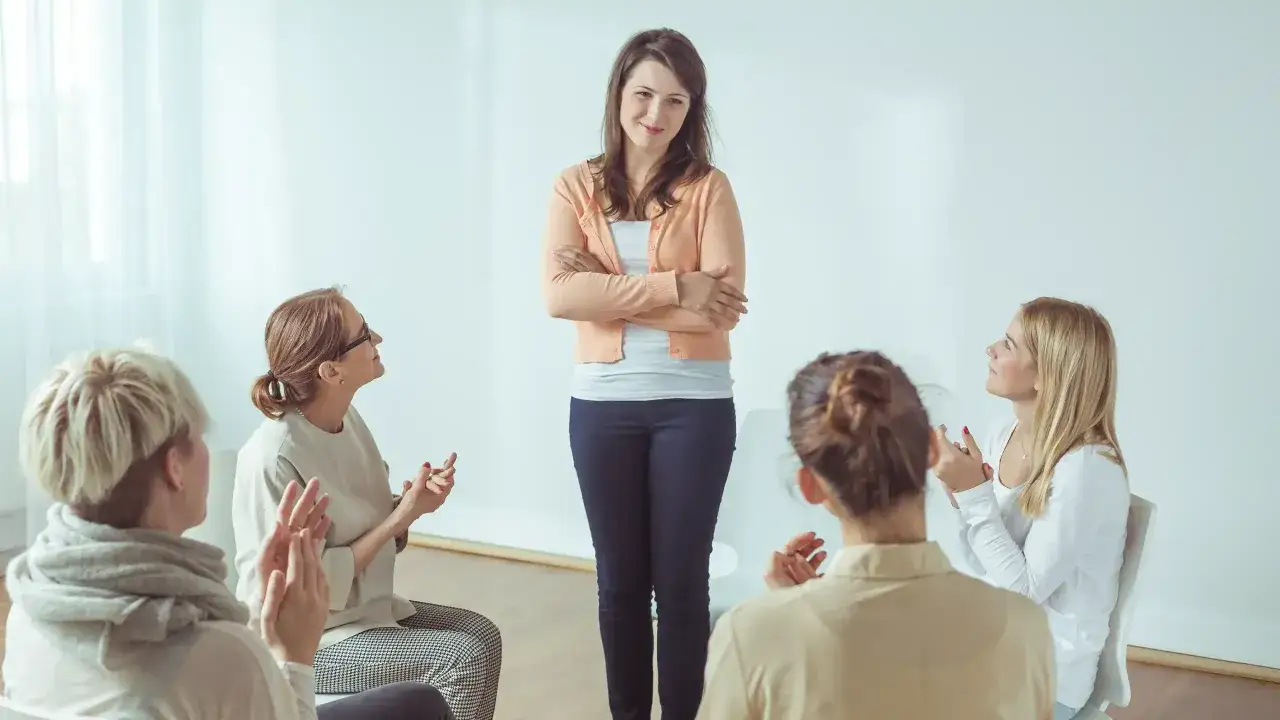 Kobieta stoi przed grupą wsparcia, która świętuje jej sukces w odwyku alkoholowym.