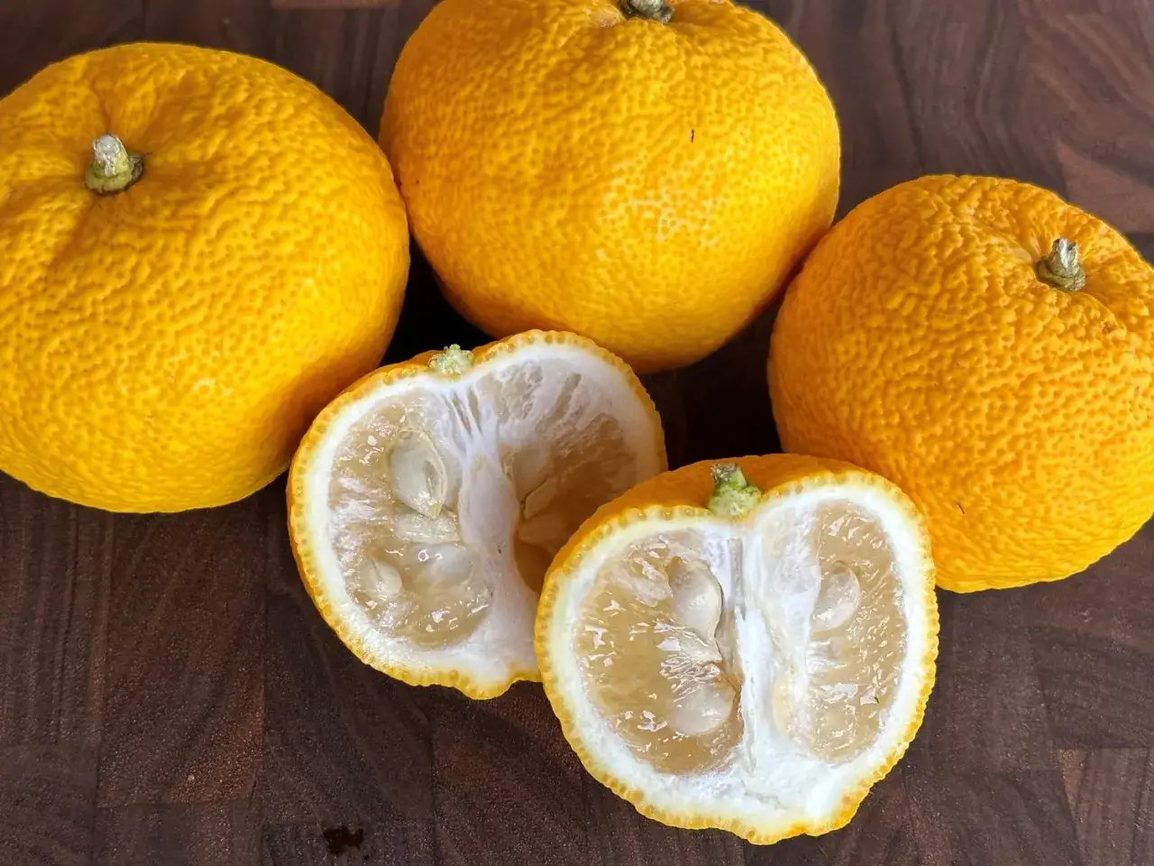Yuzu co to? Kilka całych, pomarańczowych owoców yuzu i dwa przekrojone na pół, ukazujące miąższ i pestki.