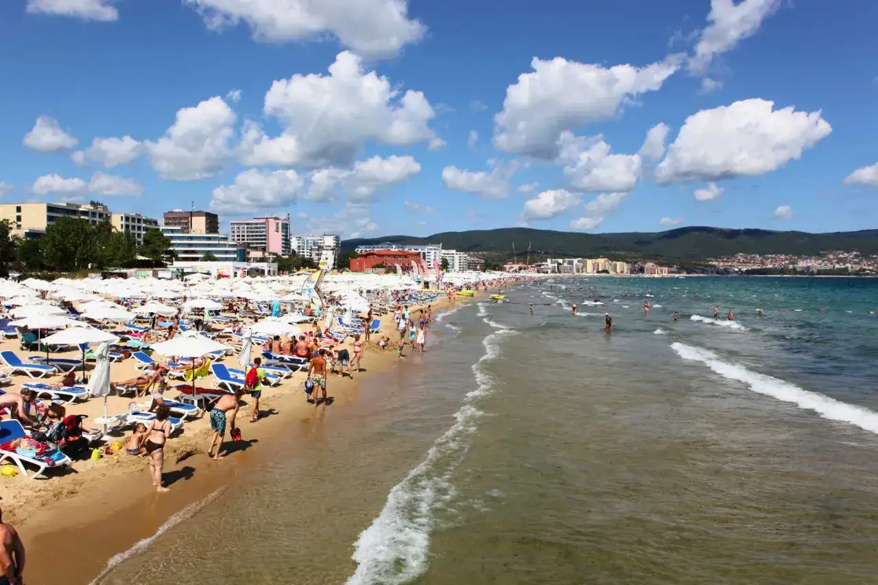 Bułgaria, Słoneczny Brzeg we wrześniu: plaża pełna ludzi, leżaki pod białymi parasolami, turkusowe morze i słoneczna pogoda.