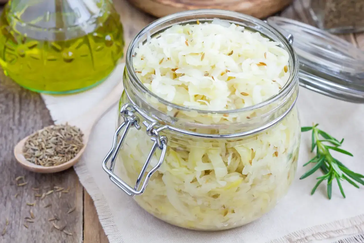 En burk med fermenterad vitk&aring;l, kryddad med kummin. Bredvid en sked med kumminfr&ouml;n och en kvist rosmarin.