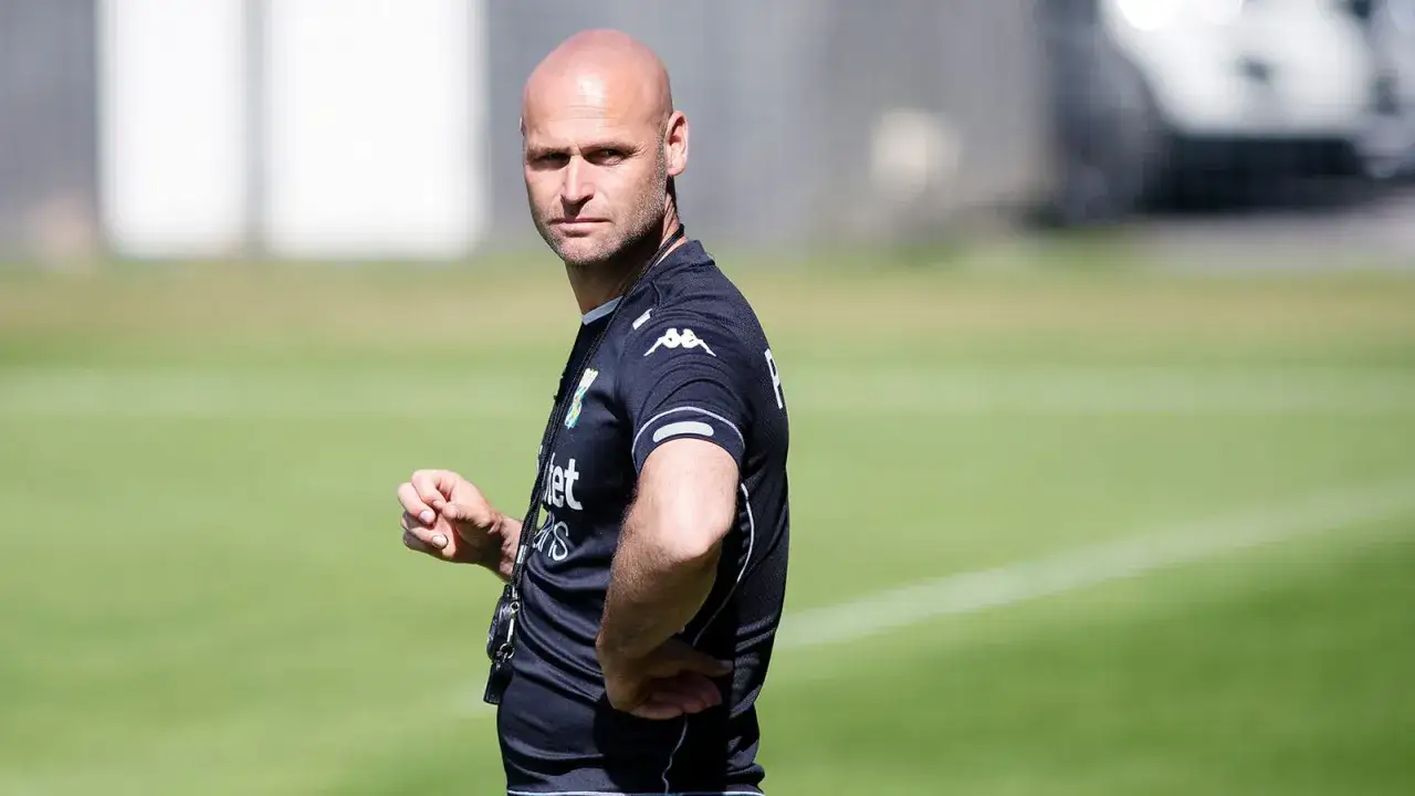 Thomas Olsson, tränare, står på en grön fotbollsplan och tittar mot kameran.