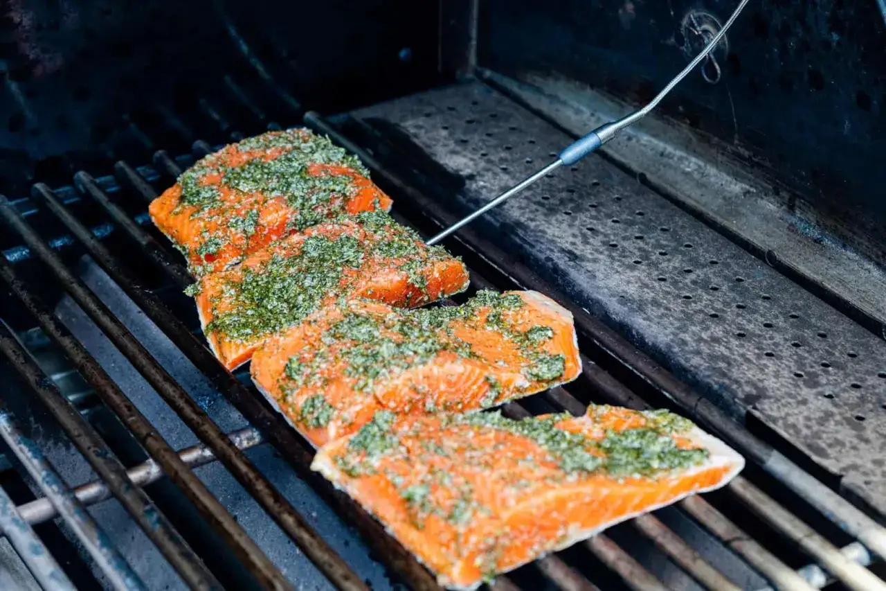 Tre saftiga laxfil&eacute;er med &ouml;rtmarinad ligger p&aring; en gasolgrill. En termometer m&auml;ter temperaturen f&ouml;r perfekt grillad lax.