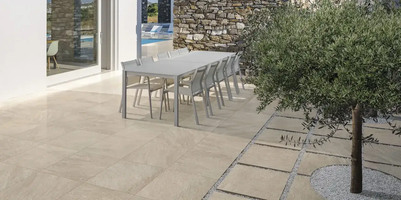 Terrazzo con pavimentazione in lastre di pietra chiara, tavoli e sedie da esterno, ulivo e piscina sullo sfondo. Schemi di posa piastrelle terrazzo.
