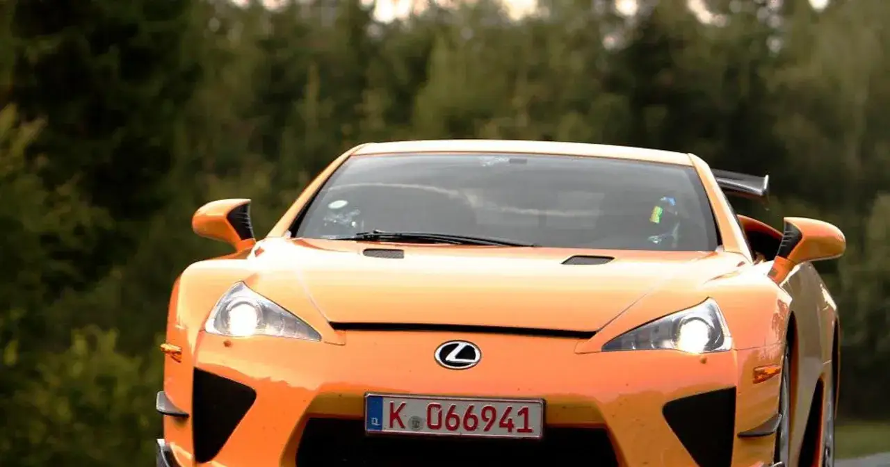Pomarańczowy Lexus LFA z tablicą rejestracyjną K 066941 pędzi po drodze wśr&oacute;d drzew.