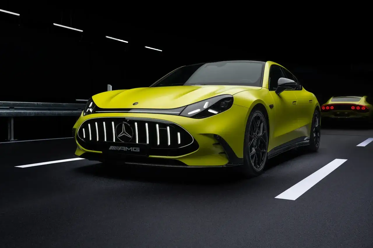 Ein leuchtend gelber AMG Elektro-Sportwagen mit beleuchtetem K&uuml;hlergrill steht auf dunklem Asphalt. Ein zweites, &auml;hnliches Fahrzeug ist im Hintergrund zu sehen.