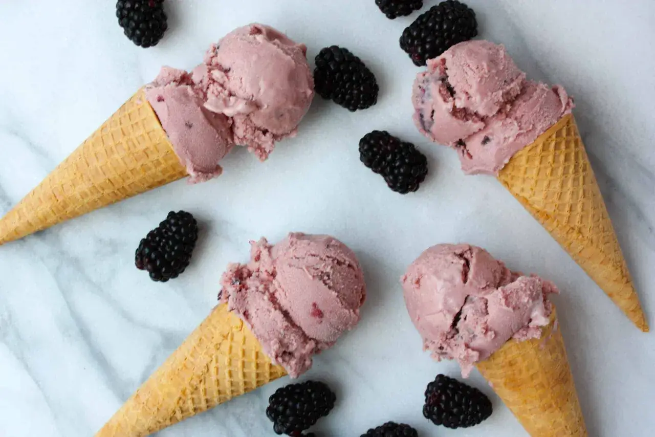 Vier Eiswaffeln mit Brombeereis, verfeinert mit Honig statt Zucker. Frische Brombeeren liegen daneben.