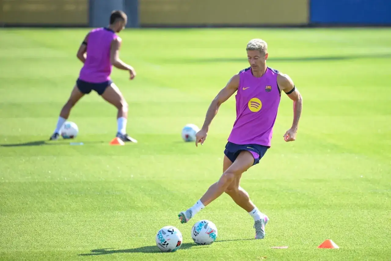 Piłkarze FC Barcelona ćwiczą na boisku. Robert Lewandowski w fioletowej koszulce i granatowych spodenkach, z piłką przy nodze, przygotowuje się do strzału. To trening w klubie kokosa.
