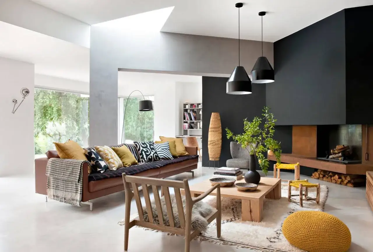 Soggiorno con divano in pelle marrone, tavolino in legno grezzo e camino moderno. L'arredamento casa moderno &egrave; completato da lampade a sospensione nere e cuscini colorati.