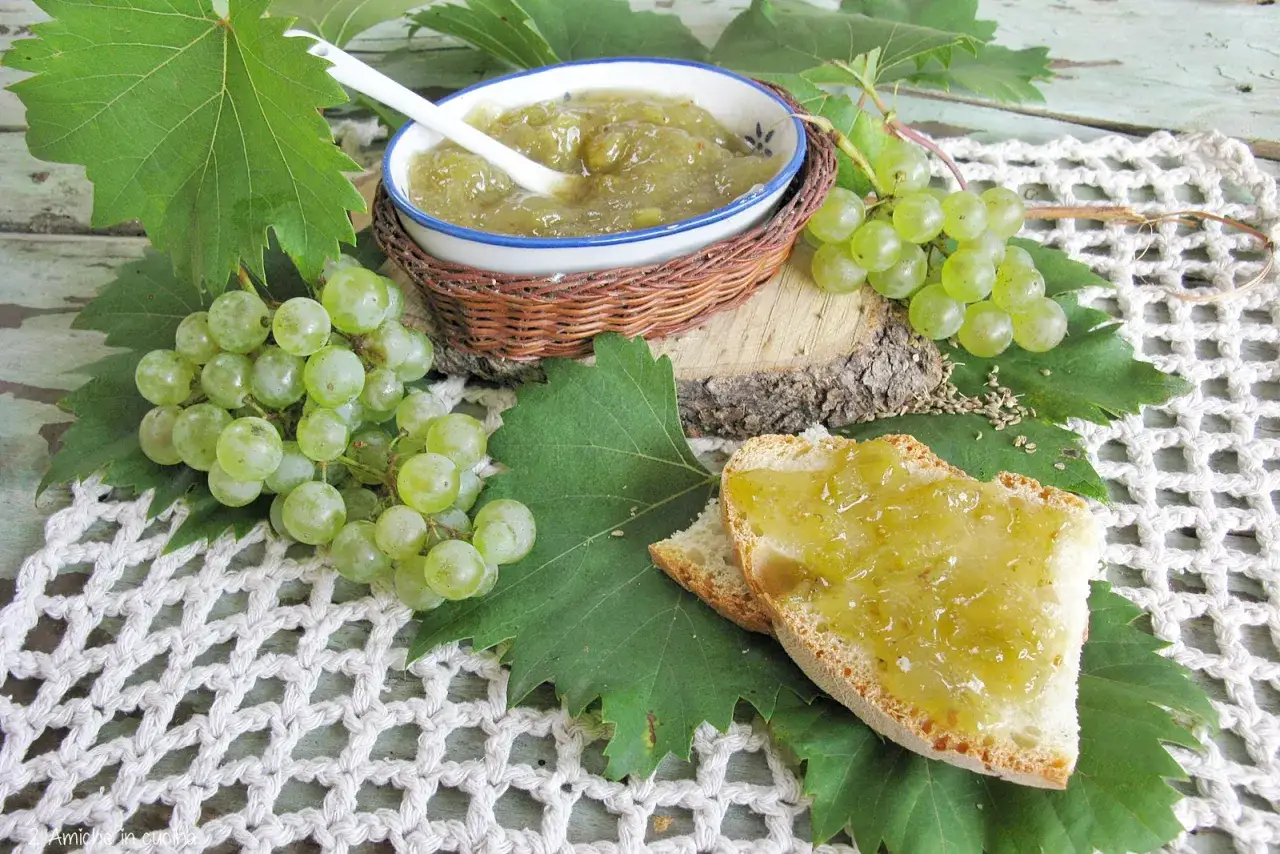 Fetta di pane con confettura di uva bianca, grappoli d'uva verde e foglie fresche su un centrino all'uncinetto.