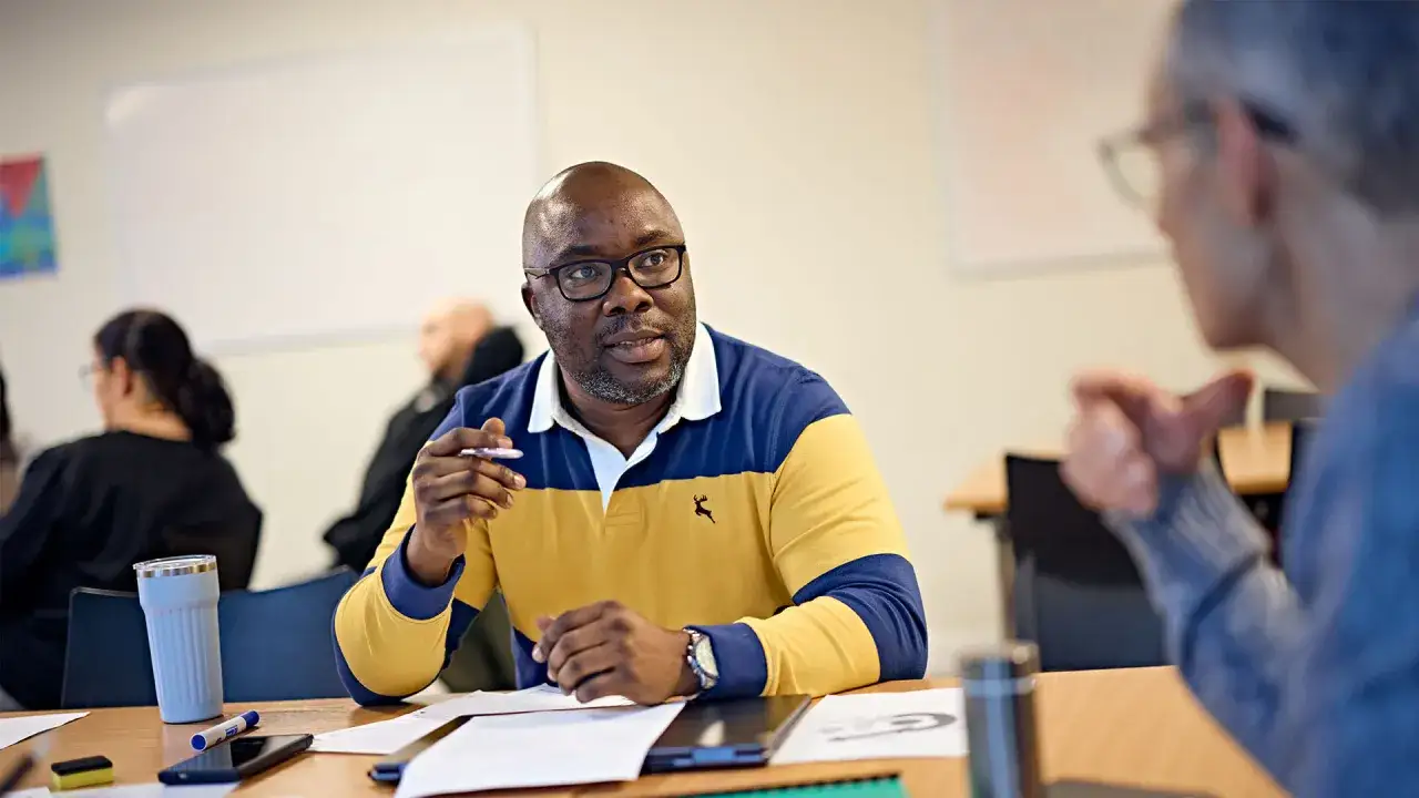 A man in a yellow and blue polo shirt, pursuing his bachelors in organizational leadership, engages in a classroom discussion.