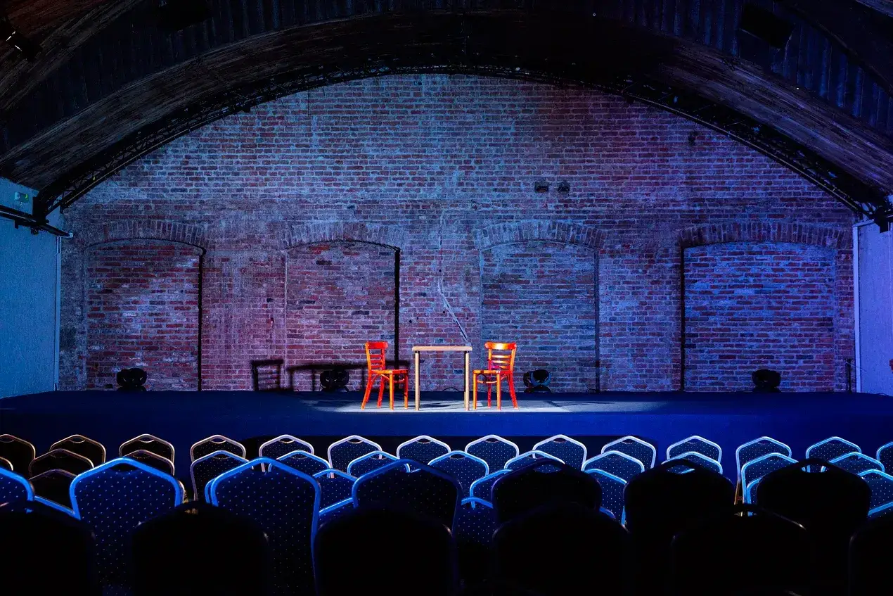 Scena teatru z dwoma czerwonymi krzesłami i stołem. Widownia czeka na spektakl. Sprawdź **teatr imka repertuar**!