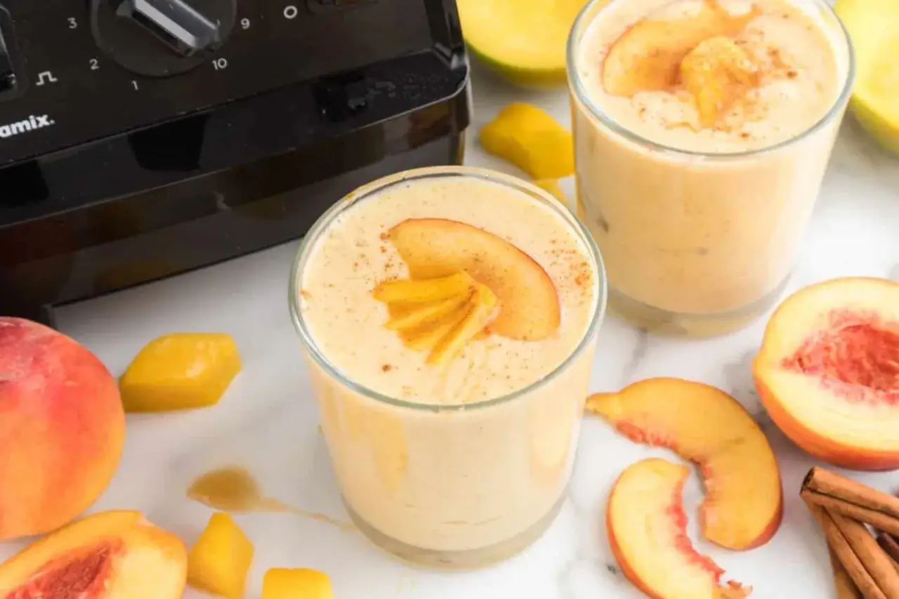 Pyszny koktajl Chodakowskiej z brzoskwini i mango, posypany cynamonem. Obok składniki i blender.