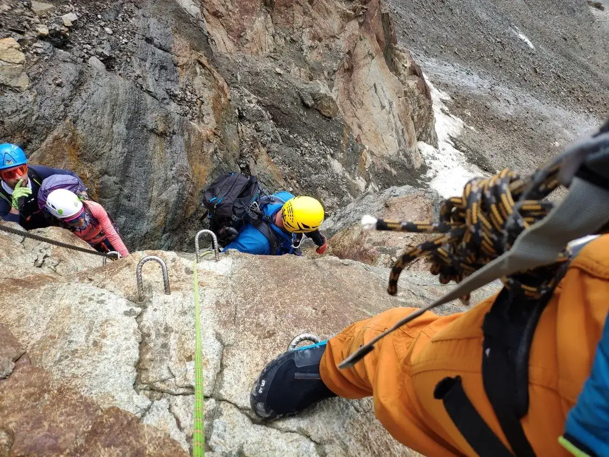 Kletterer sichern sich auf dem Weg zur Wildspitze. Ein Seil führt über Felsen, während Bergsteiger in voller Ausrüstung gesichert sind.
