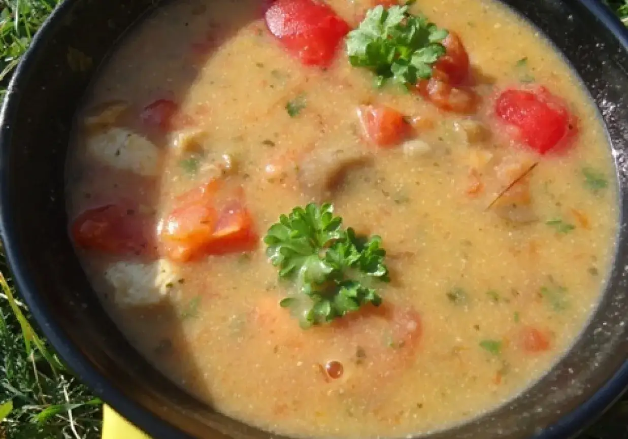 Aromatyczna zupa tom kha z kurczakiem, pomidorami i świeżą natką pietruszki, podana w czarnej misce na tle zielonej trawy.