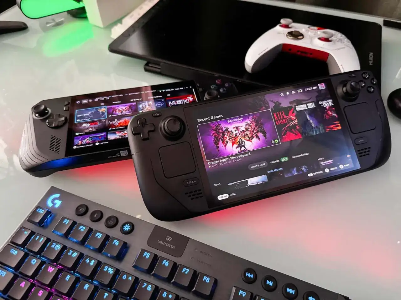 Dwa przenośne komputery do gier, w tym jeden przypominający Xbox ROG Ally X, obok klawiatury gamingowej.