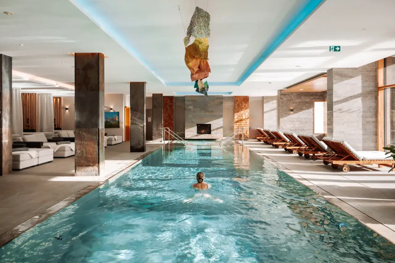 Relaks w hotelowych basenach. Kobieta pływa w basenie, obok leżaki i kominek.
