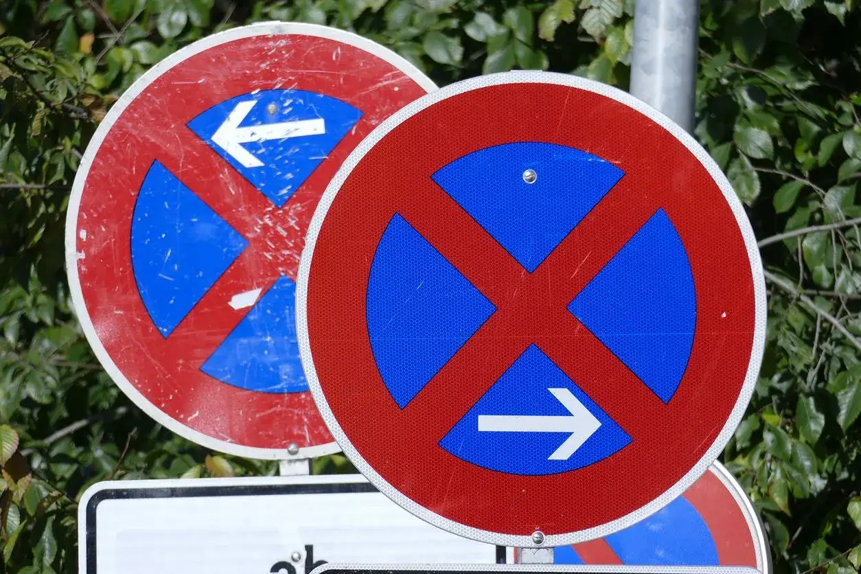 Dwa znaki drogowe w Niemczech: zakaz zatrzymywania się z niebieskim polem i białymi strzałkami wskazującymi kierunek.