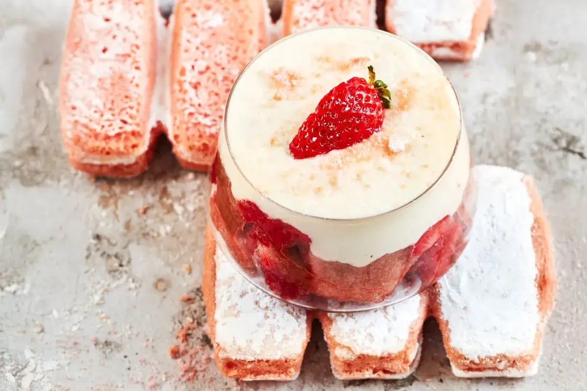 Un d&eacute;licieux tiramisu rhubarbe fraise, garni d'une fraise fra&icirc;che, entour&eacute; de biscuits roses saupoudr&eacute;s de sucre glace.