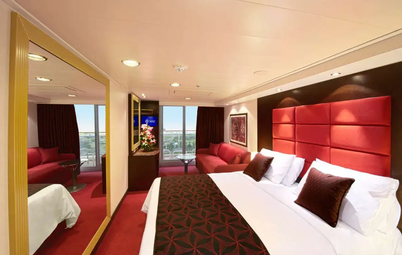 Interno di una cabina con balcone MSC Divina: letto king-size, divano rosso, specchio a figura intera e vista sul mare.