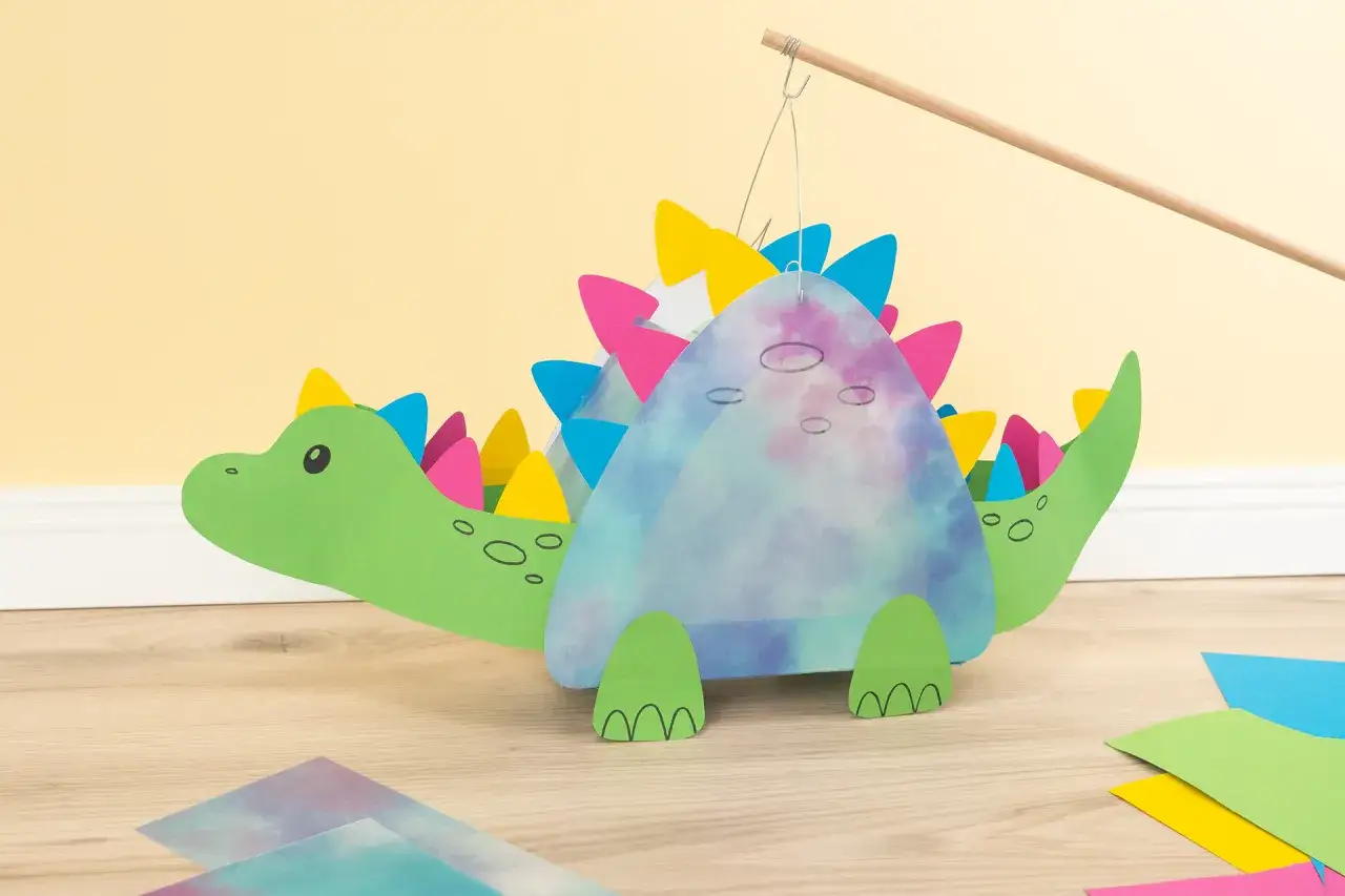Ein grüner Dinosaurier-Laternen-Bastelprozess, mit bunten Zacken und einem marmorierten Körper.