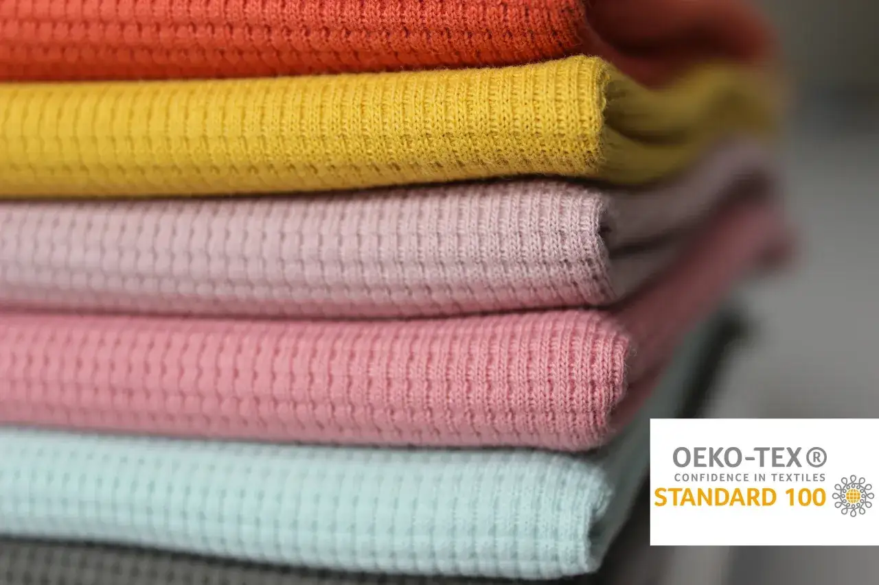 Stos delikatnych dzianin bawełnianych w pastelowych kolorach, z certyfikatem OEKO-TEX® STANDARD 100.