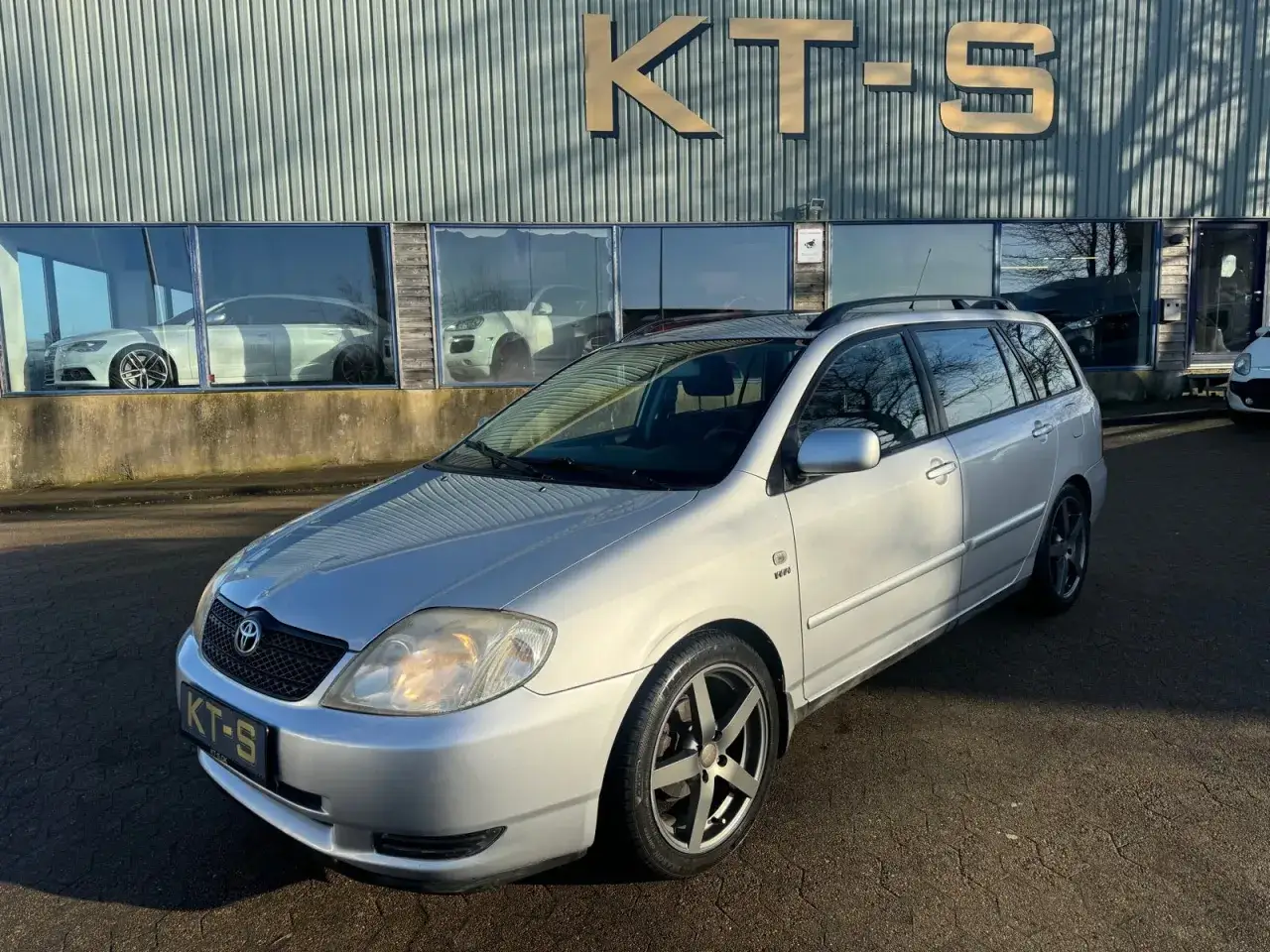 Srebrna Toyota Corolla E12 kombi stoi przed budynkiem z napisem 